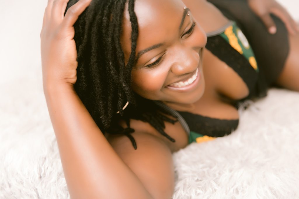 Boudoir photo of a Black woman laying in bed and smiling 