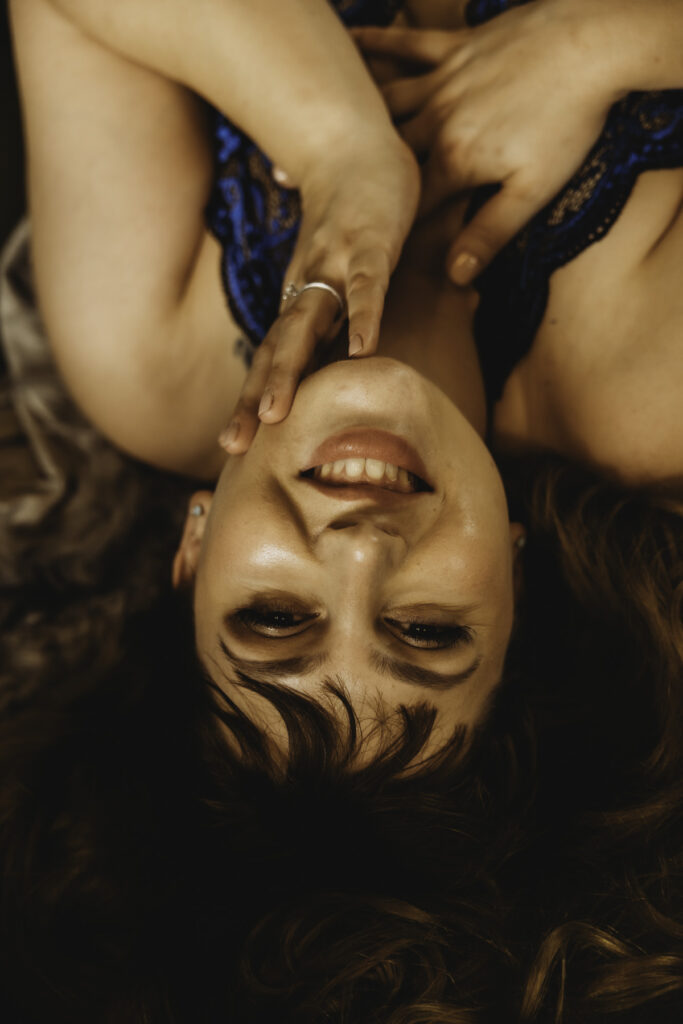 curvy boudoir session, red haired woman smiling in blue lingerie